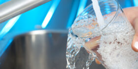 Woman filling a glass of water. She is using the faucet in the kitchen sink. She is wasting water letting the glass overflow. Close up with copy space.