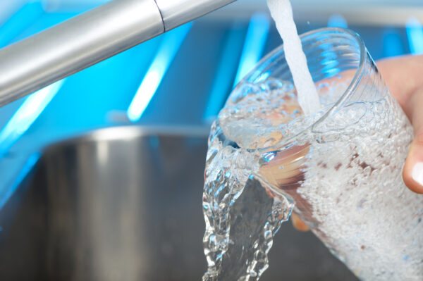 Woman filling a glass of water. She is using the faucet in the kitchen sink. She is wasting water letting the glass overflow. Close up with copy space.